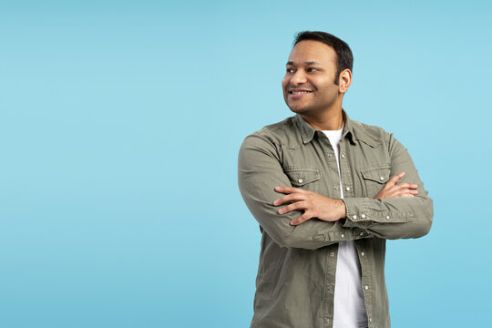 Confident indian man smiling and looking away on blue background