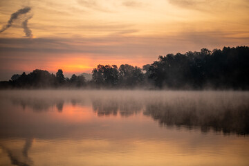 Idylische, ruhige Morgenstimmung am See zum Sonnenaufgang mit Nebel über dem Wasser