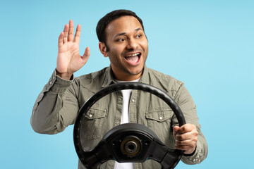 Enthusiastic driver waving hand holding steering wheel on blue background