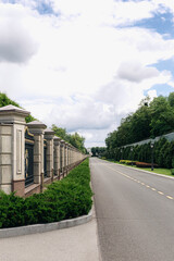 Long concrete fence with metal grating and decorative elements protecting prestigious property with green bushes and trees under cloudy sky