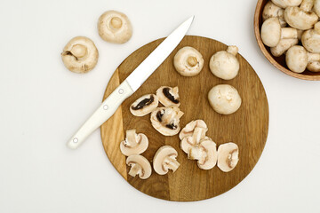 Sliced and whole mushrooms are arranged on a rustic wooden cutting board wit sharp knife, perfect for various culinary uses, preparing food.