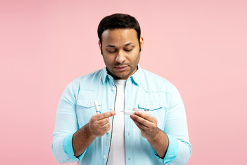 Concentrated man checking blood sugar level with glucometer on pink background