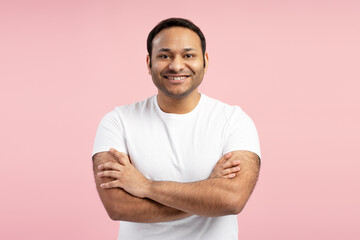 Confident indian man smiling with arms crossed on pink background