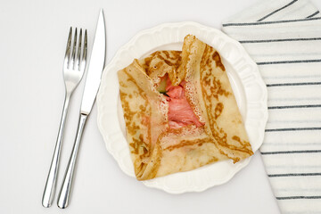 Delicious crepes with salmon, cream cheese isolated on white plate, napkin in white background.