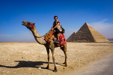 Tourist Riding a Camel in Front of the Pyramids of Giza Egypt Enjoying an Authentic Desert...