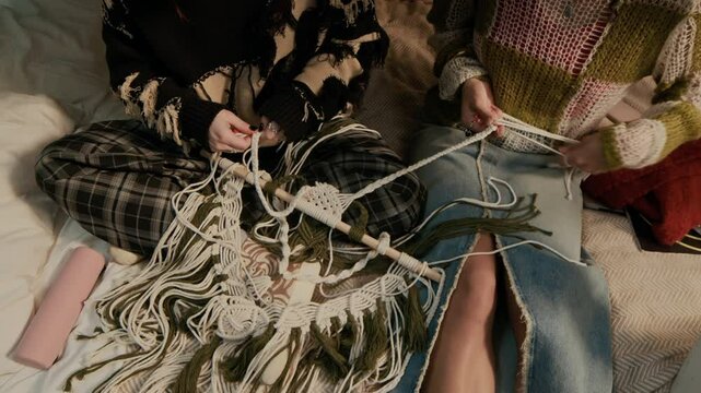 High angle view of two roommates wearing knitted jumpers making home decor using macrame pattern in dorm room