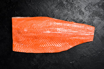 Half raw salmon or trout fillet on dark stone surface. Top view.