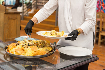 A waiter in a white suit and black gloves neatly arranges on plates the pilaf just cooked by Shah.