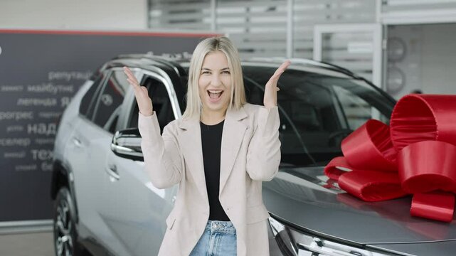 Woman stands confidently near a car with a large bow in a showroom promoting test drives and purchases