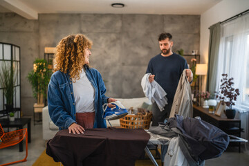 Fototapeta premium A woman iron shirts on an ironing board, while a man folds up them
