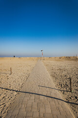 Paved walkway leading to sandy beach under clear sky