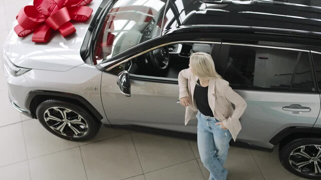 Excited woman prepares for test drive of a stylish car with a large bow in a welcoming showroom