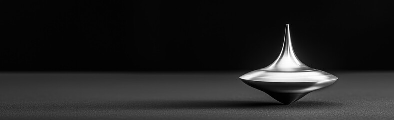 Fototapeta premium A sleek metal spinning top in motion on a dark textured surface, with a dramatic black background. Balance and uncertainty concept. Ideal for desktop wallpaper background.