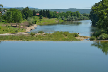A dam on the Kupa River in Ozalj, Croatia, creates a calm pool of water reflecting the clear blue sky