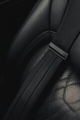 A detailed view of a black seatbelt on a textured leather car interior.