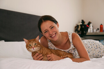 Young woman playing with her rescue red cat in bed. Copy space background.