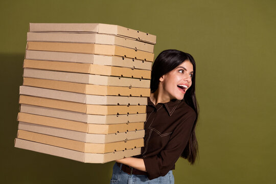 Young woman happily carrying many pizza boxes against a khaki background