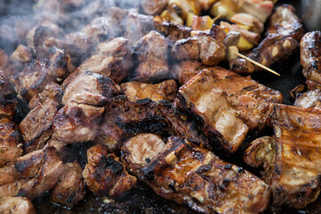Close-up of many pieces of meat grilling on a barbecue outside. Lots of meat on the barbecue with smoke in a distinct texture. Street food festival.