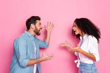Young couple engaged in animated discussion against pink background showcasing lively emotions