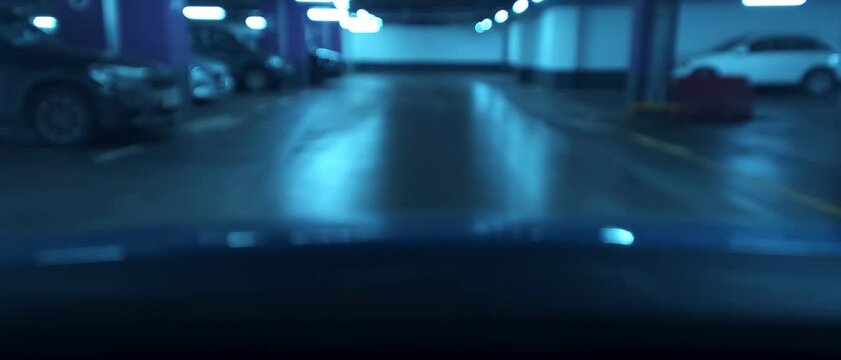 Blurred view of empty underground parking garage with parked cars and neon lights
