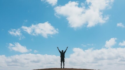 Silhouette of a man with arms raised against a bright blue sky and fluffy clouds.