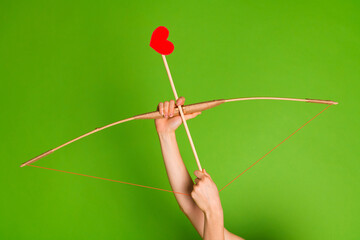 Fototapeta premium Hands holding a bow and arrow with red heart symbol on green background, love and Valentine's Day concept.