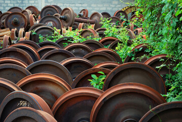 Rusty metal wheels stacked outdoors overgrown with vegetation
