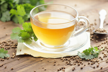Coriander seed tea in a glass cup with cilantro herb on wooden rustic background, closeup, heart and skin healing drink, natural medicine and naturopathy concept