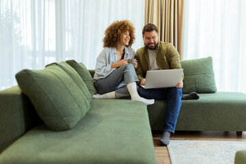 Obraz premium Couple sharing a joyful moment while exploring ideas on a cozy green couch in a sunlit living room