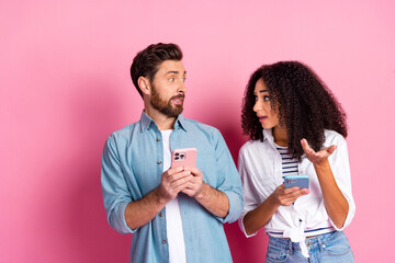 Young couple discussing over smartphones in a casual setting with pink background
