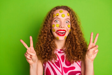 Cheerful young woman with vibrant red hair in stylish fashion smiling with emoticon stickers on face making peace gestures