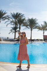 Obraz premium A stylish woman is enjoying a beautiful sunny day by the shimmering pool surrounded by lush palm trees