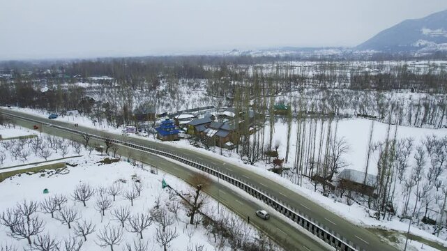 aerial drone shot flying slowly forward at Tanmarg Kashmir with colorful houses in between barren trees and the busy gulmarg srinagar highway in front