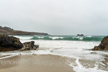Une vague émeraude déferle sur la plage de Pors Péron en Bretagne, laissant une écume blanche scintiller sur le sable mouillé.