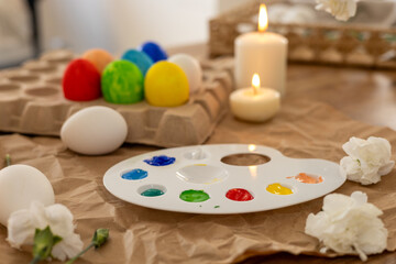 Colorful Easter eggs being painted on a spring day with candles and flowers nearby