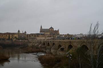The Roman Bridge of Córdoba crossing the Guadalquivir River, with the iconic Mosque-Cathedral in the background, a breathtaking blend of history and architecture in Andalusia, Spain