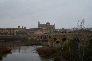 The Roman Bridge of Córdoba crossing the Guadalquivir River, with the iconic Mosque-Cathedral in the background, a breathtaking blend of history and architecture in Andalusia, Spain