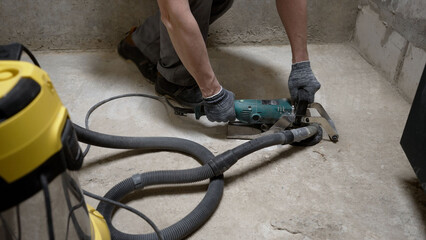 Construction worker removing excess concrete with angle grinder and vacuum cleaner