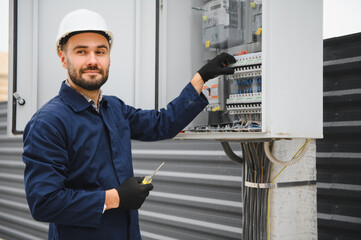 Joyful electrician mounting electric switchboard outdoors
