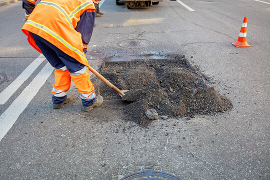Road workers repair pothole in bright orange uniforms on a busy street. Copy space.