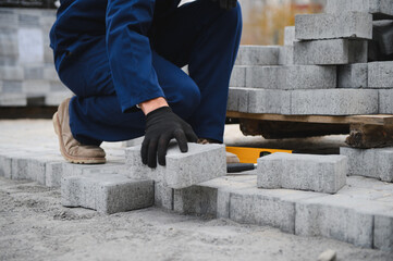 The master in gloves lays paving stones in layers. Garden brick pathway paving by professional paver worker. Laying gray concrete paving slabs in house courtyard on sand foundation base