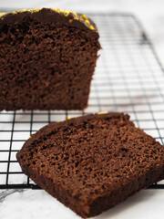 Sliced cake on a cooling rack with a bigger cake on the side. White marble counter as a background