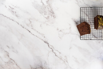 Sliced cake on a cooling rack with a bigger cake on the side. White marble counter as a background