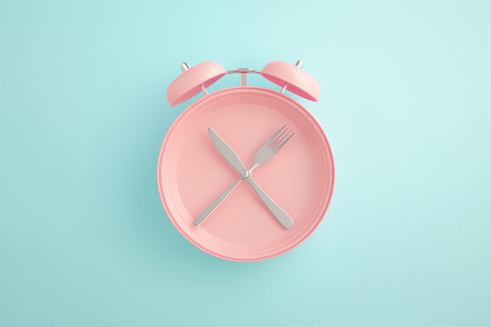Alarm clock and plate with cutlery . Concept of intermittent fasting, lunchtime, diet and weight loss 
