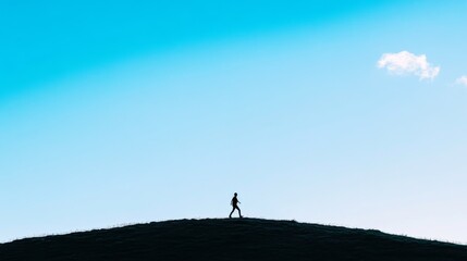 Silhouette of a person walking on a hill against a vibrant blue sky.