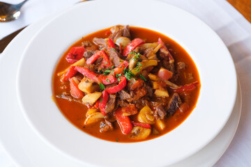 Hearty stew with chunks of meat red peppers and mushrooms in a rich tomato broth