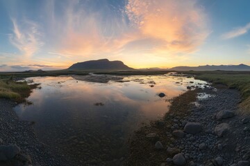 Obraz premium Sunset reflecting on a calm river with rugged mountains in the background and wispy clouds in a clear sky