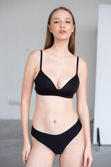 Fototapeta premium Professional modeling digitals of a young female model in black lingerie, standing confidently in a clean studio setting. Capturing natural beauty, symmetry, and elegance for agency submission