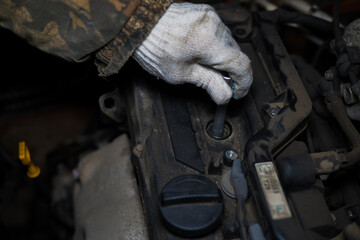 Auto mechanic wearing gloves and using a spark plug wrench is replacing spark plugs on a dirty car...