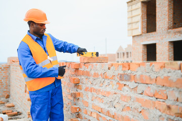 African american Bricklayer industrial worker installing brick masonry on exterior wall with trowel...